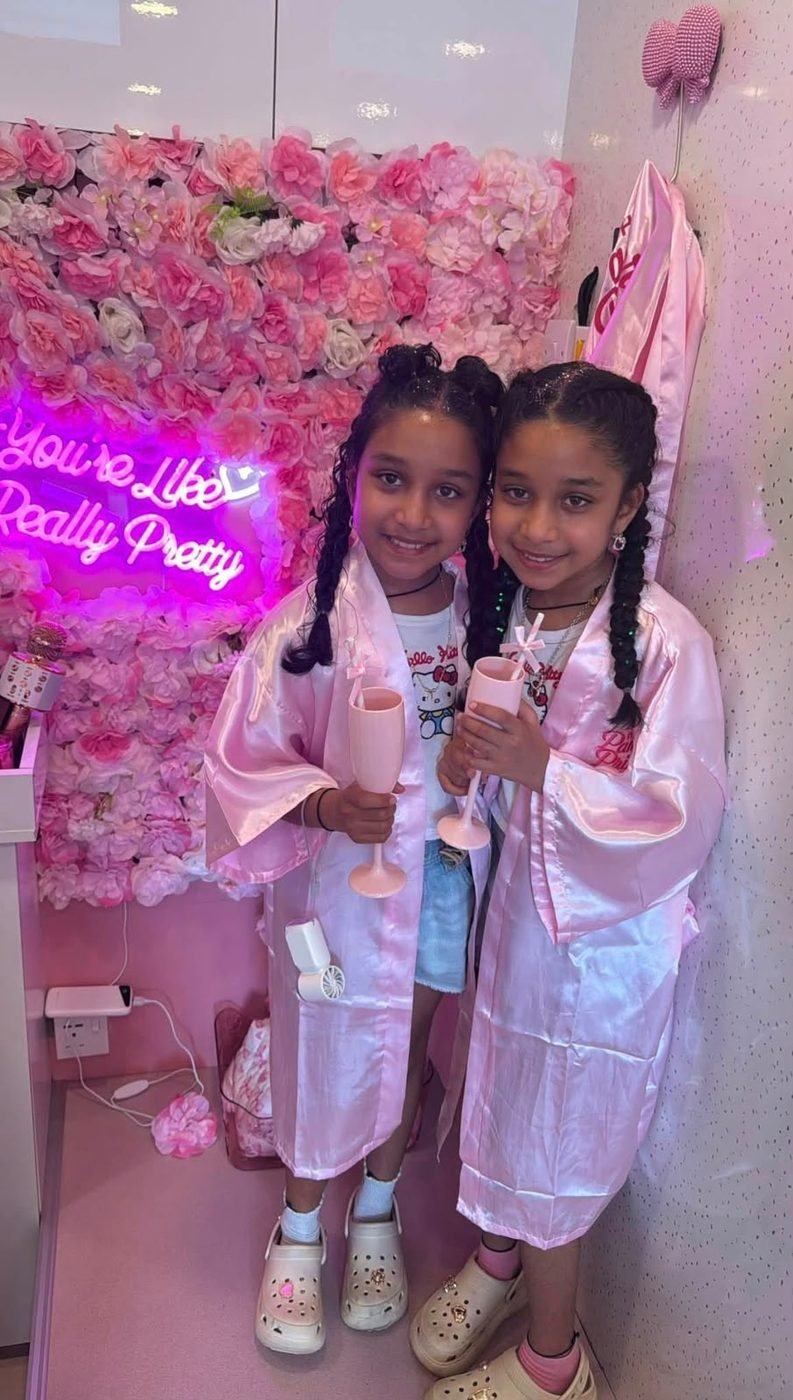 Two girls with mocktails in front of the flower wall and neon sign